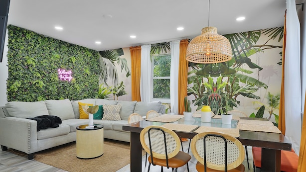 A modern living room with a sofa, dining table, chairs, and a wall mural. - 28 Guest - 4 Kitchens. Jungle Retreat in Heart Wynwood (Miami)