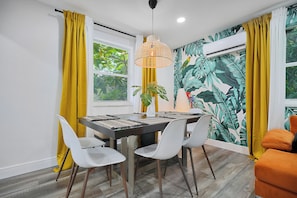 Un coin repas avec une table dressée pour quatre personnes, des chaises blanches et un luminaire suspendu.