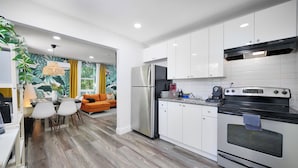 A modern kitchen with white cabinets, stainless steel appliances, and a dining area with a table and chairs. - 28 Guest - 4 Kitchens. Jungle Retreat in Heart Wynwood (Miami)