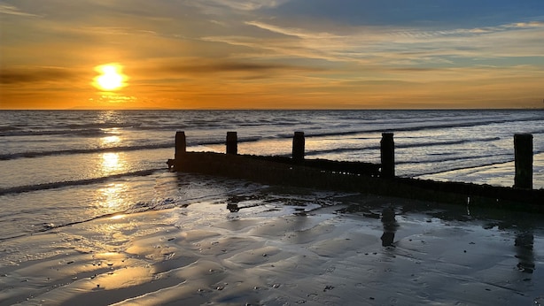 Ein Sonnenuntergang über einem Strand, mit einem hölzernen Steg, der sich ins Wasser erstreckt.