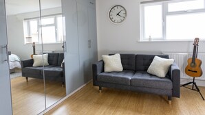 Ein modernes Wohnzimmer mit einem grauen Sofa, einem großen Spiegel, einer Uhr und einer Gitarre.