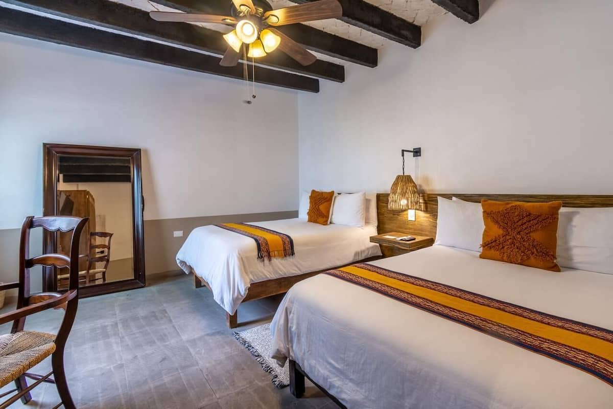 Ein Hotelzimmer mit zwei Betten, einem Deckenventilator, einem Holzstuhl und einem Tisch.