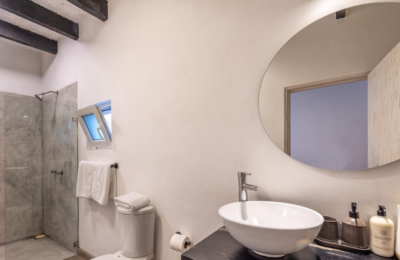 Un baño moderno con un espejo redondo grande, un lavabo blanco y una zona de ducha.