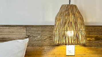 A bed with a white pillow, a wooden headboard, and a wall-mounted lamp with a woven shade.
