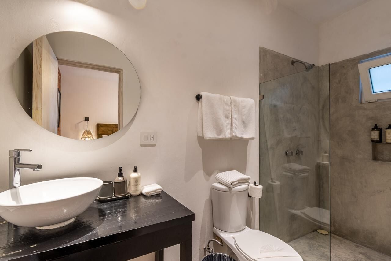 Une salle de bain moderne avec un miroir rond, un plan de toilette noir, un lavabo blanc et une douche à parois de verre.