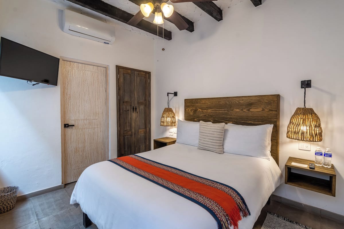 Ein Schlafzimmer mit einem großen Bett, einem Holzkopfstück, zwei Nachttischlampen, einem Nachttisch und einem an der Wand montierten Fernseher.
