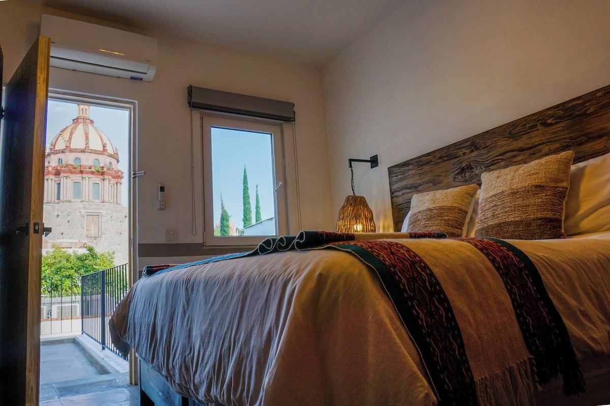 Ein Schlafzimmer mit einem großen Bett, einem Fenster mit Blick auf ein Gebäude und einem Balkon.