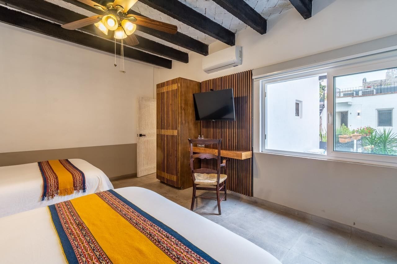 A hotel room with a bed, a desk, a television, and a window with a view of the outside.