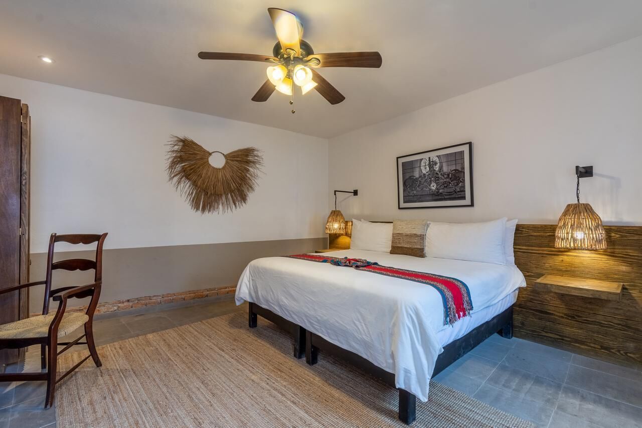 A bedroom with a bed, a ceiling fan, a wall-mounted lamp, and a framed picture.