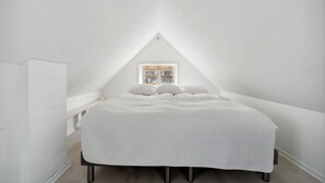 A white, triangular attic bedroom with a bed, a small window, and a white wall. - 1 bedroom cozy home in Svaneke (Svaneke)
