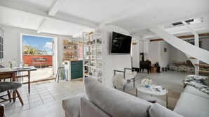 A spacious living area with a sofa, a dining table, and a kitchen area with shelves and a TV. - 1 bedroom cozy home in Svaneke (Svaneke)