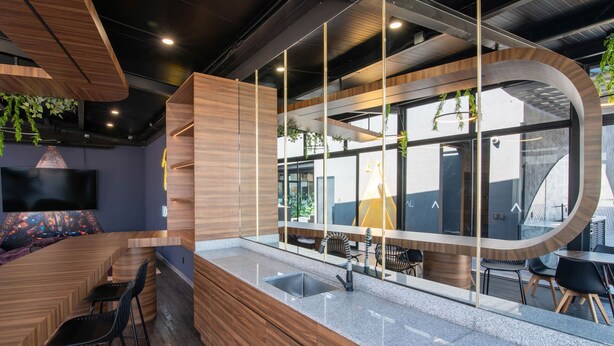 A modern interior with a wooden reception desk, a glass partition, and a seating area with black chairs. - Be Local Lofts & Coworking (Mexico City)