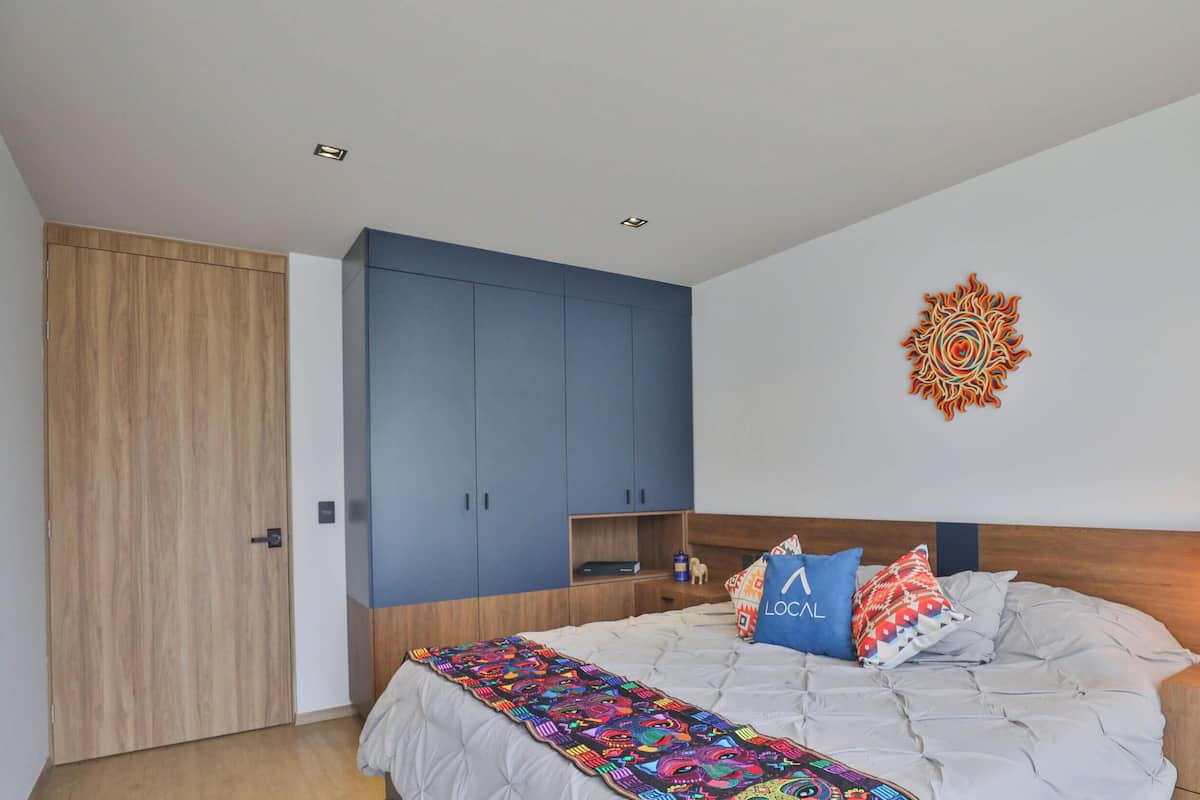 Ein Schlafzimmer mit Bett, Kleiderschrank, Nachttisch, Lampe und Wandbild.
