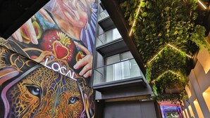 An interior corridor with a vibrant mural, a green wall with hanging plants, and a neon sign reading "LOCAL". - Be Local Lofts & Coworking (Mexico City)