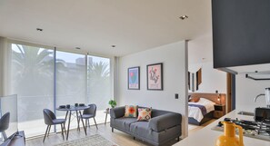 Un apartamento moderno con balcón, zona de comedor, sala de estar con sofá y televisión, y cocina con estufa.
