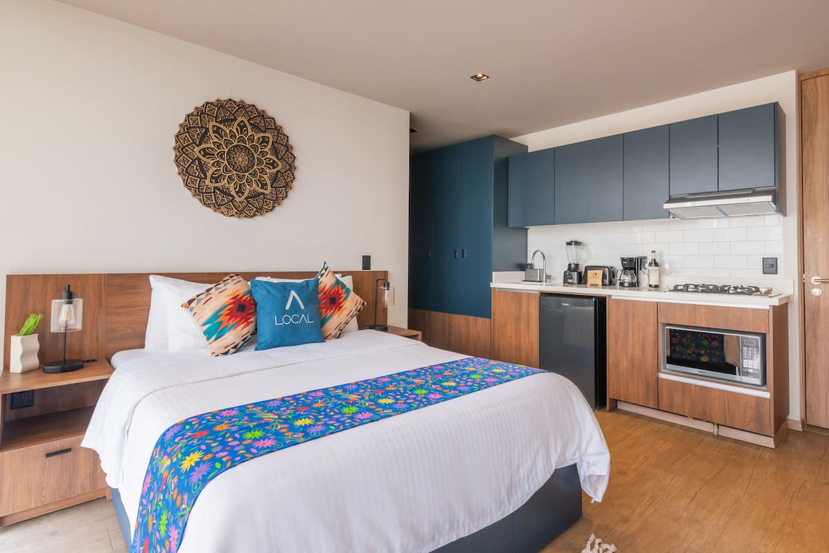 Ein modernes Hotelzimmer mit einem großen Bett, einer kleinen Küchenzeile und einem dekorativen Wandbild.