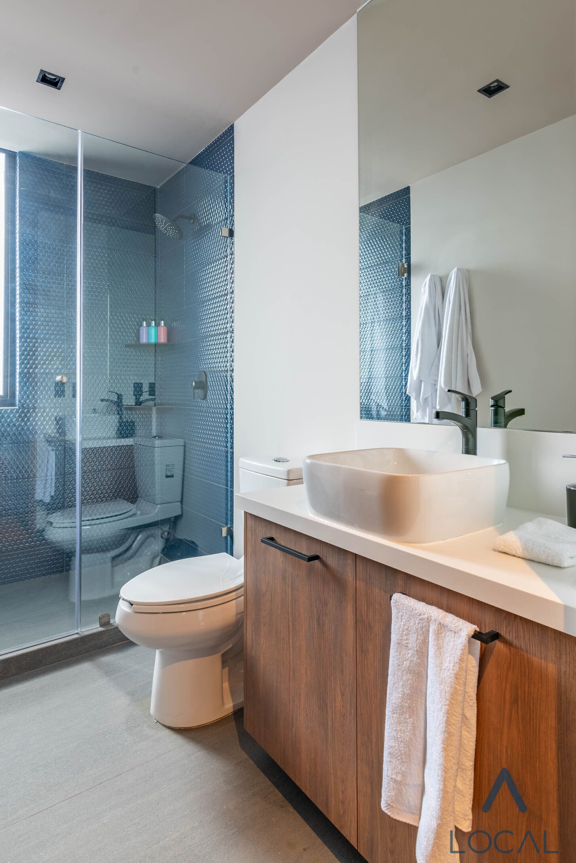Un baño moderno con cabina de ducha de vidrio, un lavamanos grande y un mueble de tocador de madera.