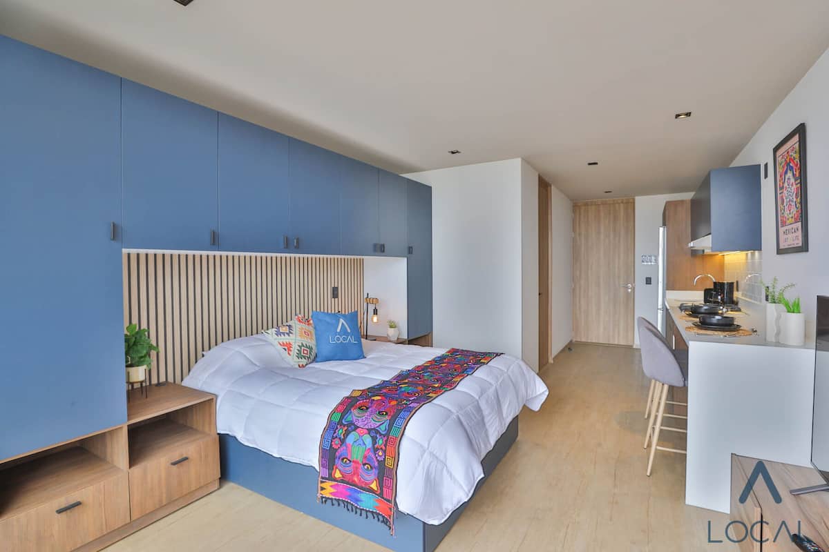 Ein modernes Schlafzimmer mit Bett, Schreibtisch und einer Küchenzeile.