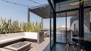 A modern outdoor seating area with a patterned floor, a glass door leading to an interior space, and a view of the cityscape. - Be Local Lofts & Coworking (Mexico City)