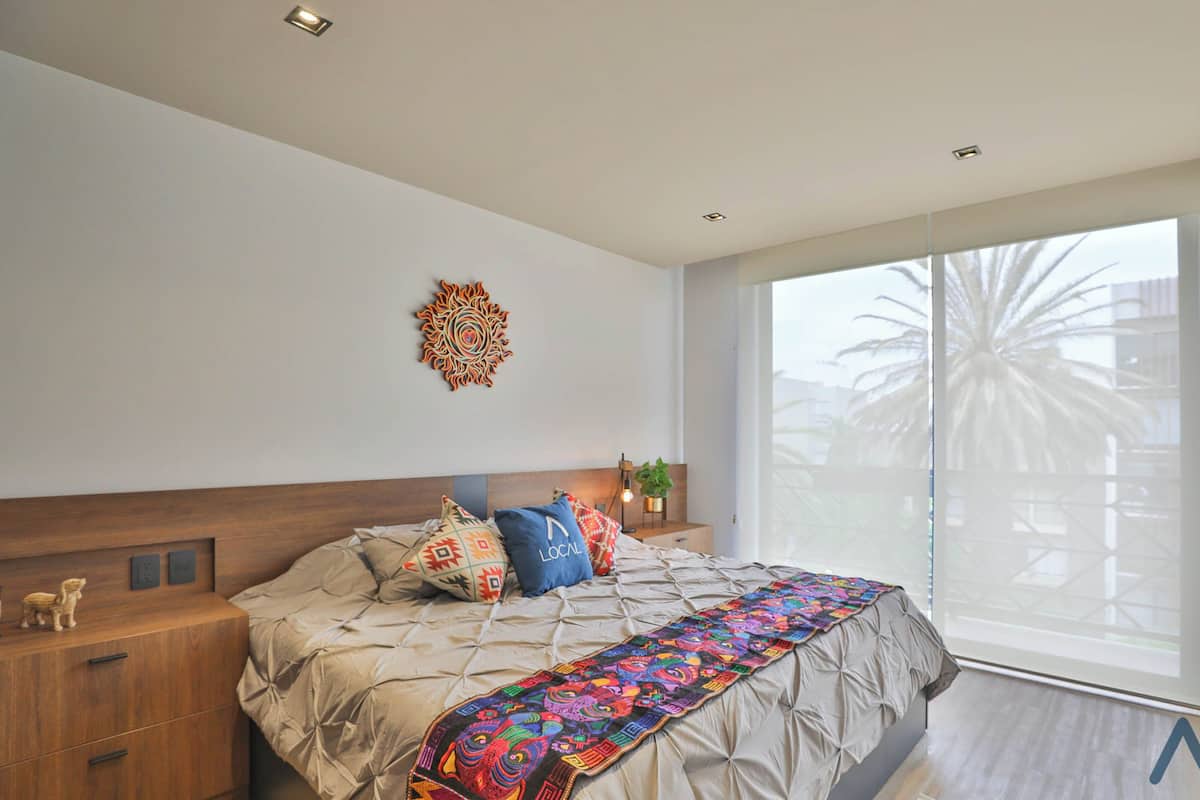 Ein Schlafzimmer mit Bett, Nachttisch, Wanddeko und Blick auf Palmen durch eine Schiebetür.