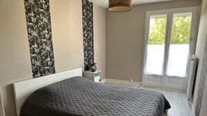 A bedroom with a large bed, a nightstand, a lamp, and a window with a view of greenery.