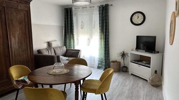 A dining area with a wooden table and yellow chairs, a sofa, and a television on a white stand.
