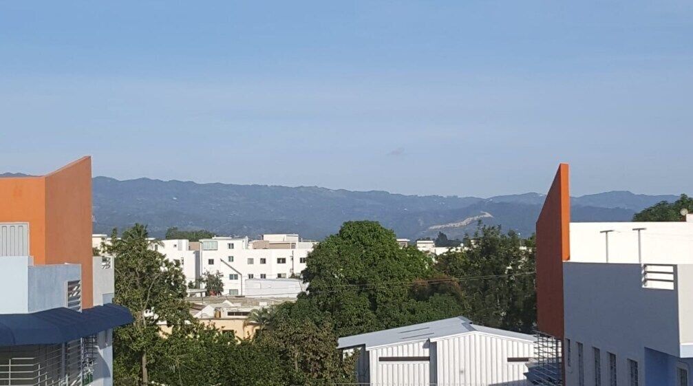 Un paisaje urbano con edificios modernos, cielo despejado y montañas a lo lejos.