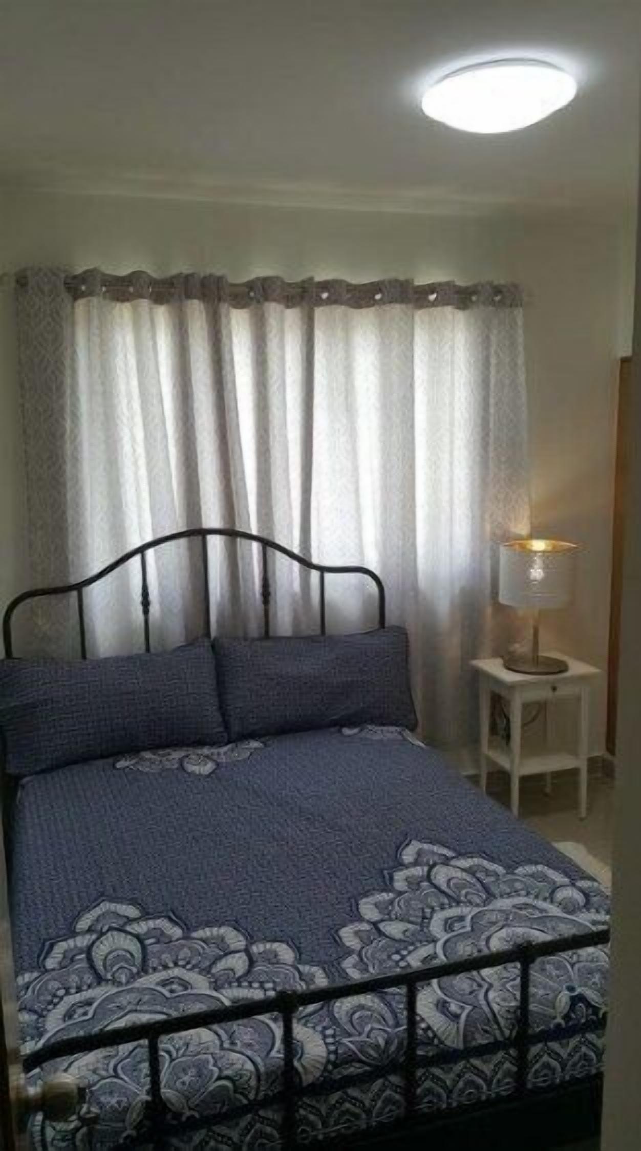 A bedroom with a bed, curtains, a nightstand, and a lamp.