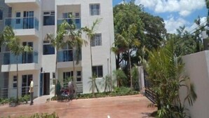 Un edificio moderno de varios pisos con balcones, rodeado de vegetación y un cielo despejado.