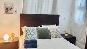 A neatly made bed with patterned pillows, a bedside lamp, and a small plant on a nightstand. - Comfortable 3 Rooms with pool, Wifi, 1st level (Santiago De Los Caballeros)