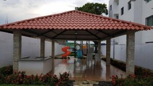 A covered outdoor area with a tiled roof, surrounded by a low stone wall and small plants. - Comfortable 3 Rooms with pool, Wifi, 1st level (Santiago De Los Caballeros)
