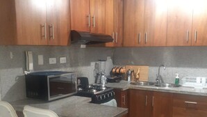 A kitchen with wooden cabinets, a microwave, a stove, and a sink. - Comfortable 3 Rooms with pool, Wifi, 1st level (Santiago De Los Caballeros)