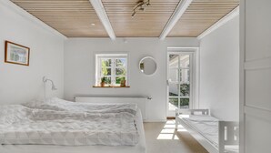 A bedroom with a large bed, a smaller bed, a window with a view, a circular mirror, and a wall-mounted lamp. - Gorgeous home in Bogense with WiFi (Bogense)