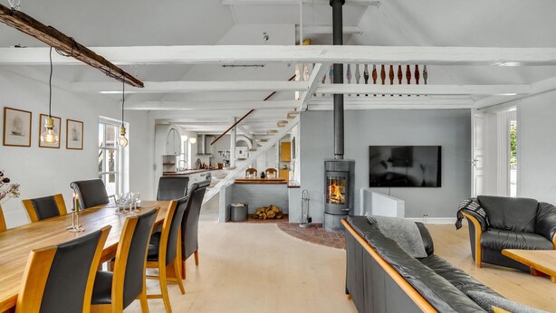 A spacious living area with a long wooden dining table, comfortable seating, a fireplace, and a staircase leading to an upper level. - Gorgeous home in Bogense with WiFi (Bogense)