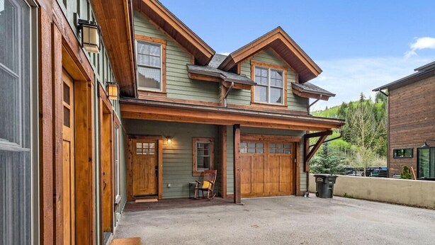 A two-story building with a covered front porch, wooden doors, and a gravel driveway.
