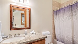Une salle de bain avec un lavabo sur un plan de travail en granit, un miroir encadré en bois et un rideau de douche à motifs géométriques.