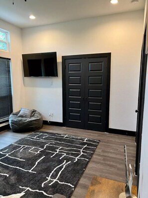 A room with a black door, a mounted TV, a bean bag chair, and a patterned rug. - Modern Farmhouse 3-bedroom home, Luxury Master (DeSoto)