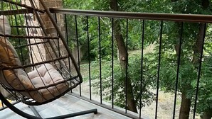 Un balcon avec un fauteuil suspendu, un sol en pierre et une vue sur les arbres.