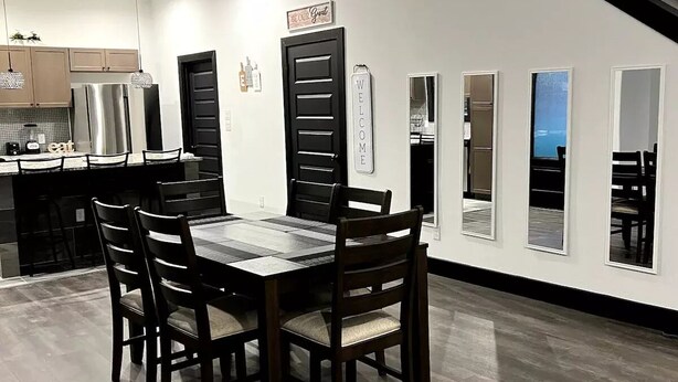 Une cuisine moderne avec un coin repas, comprenant un grand îlot central, des chaises en bois foncé et une porte à cadre noir.