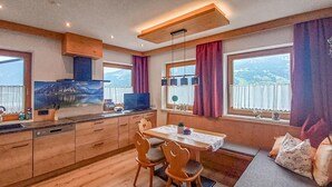 Une cuisine moderne avec des meubles en bois, une table à manger avec des chaises et une vue sur les montagnes grâce à de grandes fenêtres.