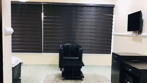 A room with a black leather chair, a TV mounted on the wall, and a large window with blinds. - T Golden Villa Hotel (Enugu)