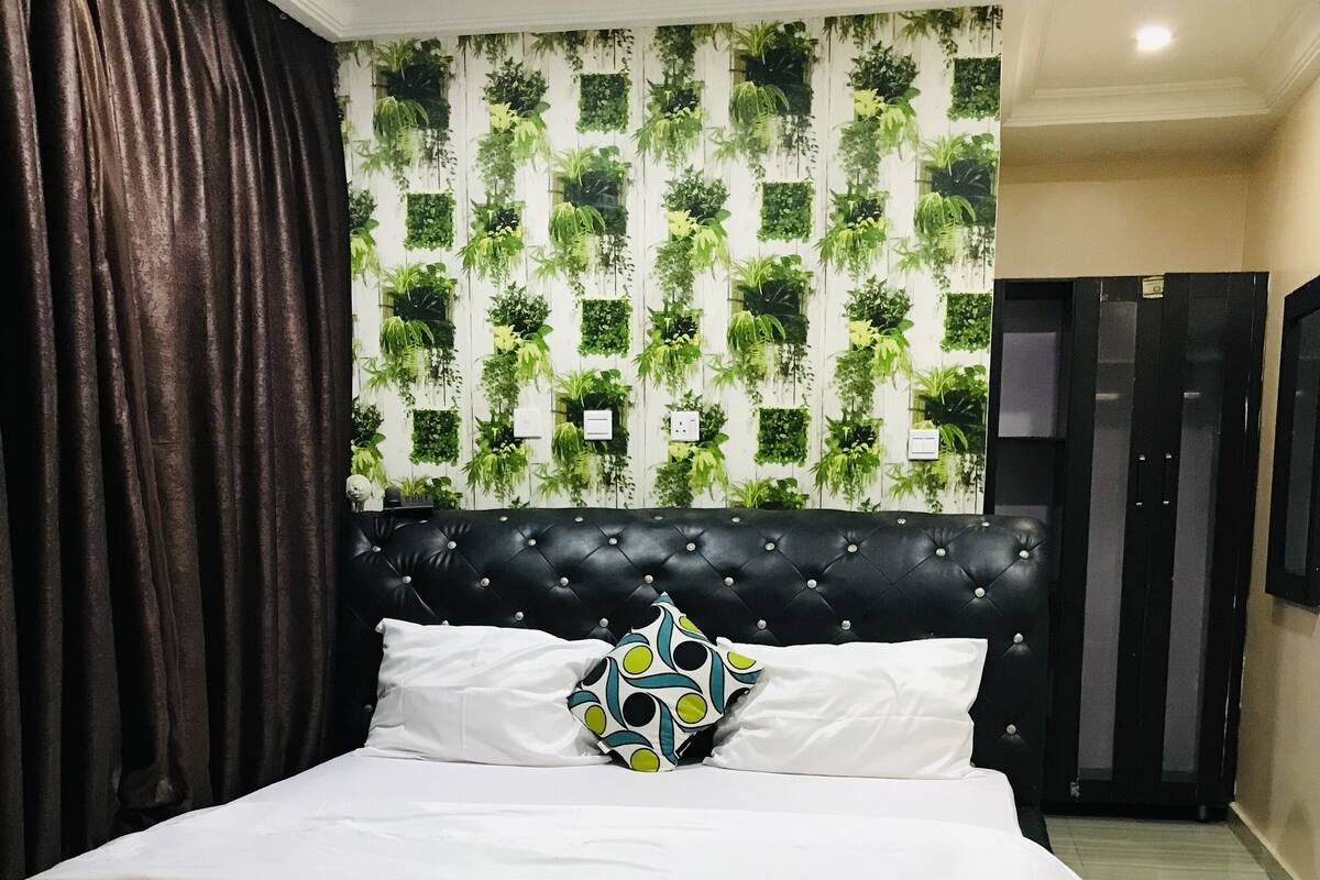 A bedroom with a black tufted headboard, white bedding, and a decorative pillow.