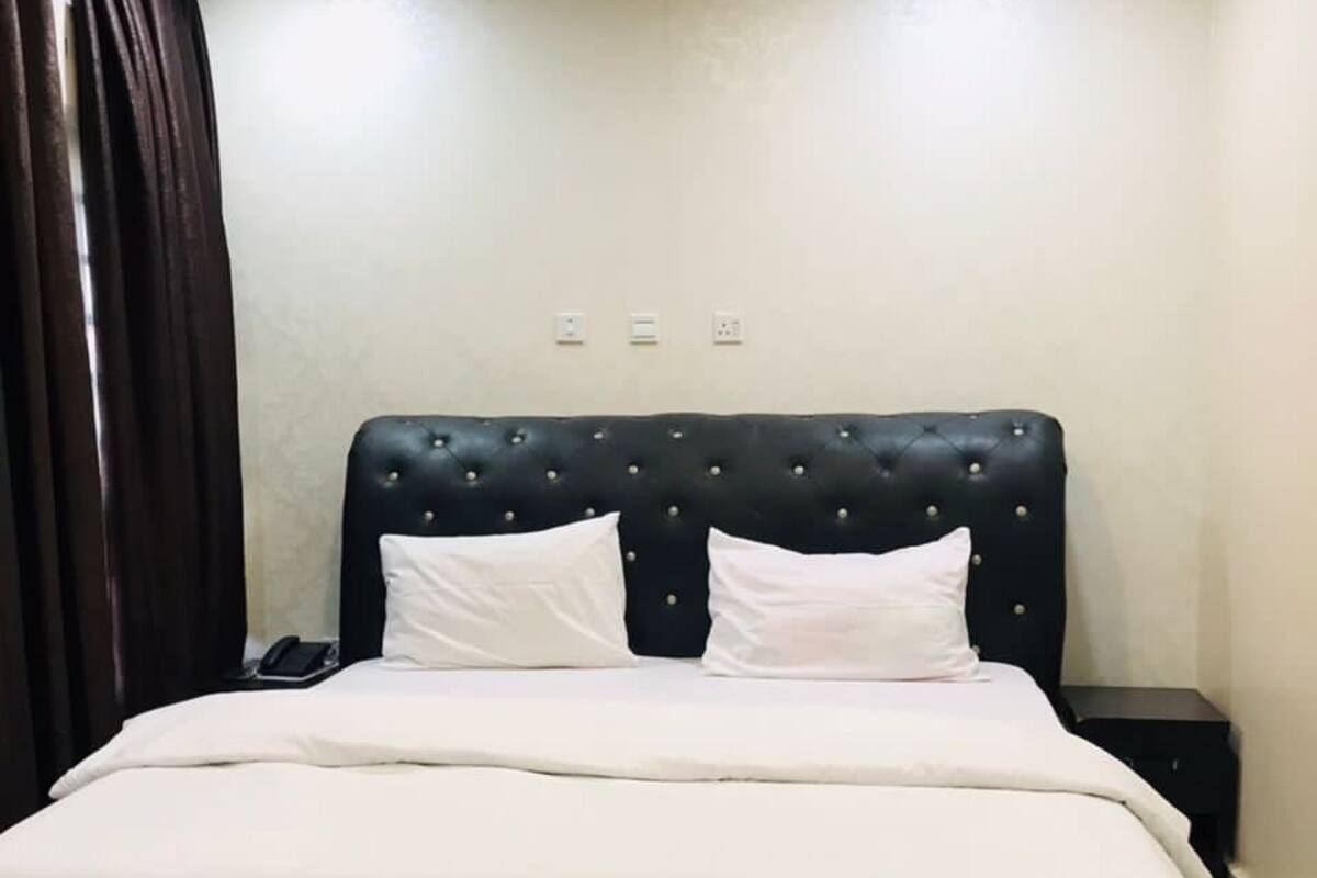 A neatly made bed with white linens in a room with a dark headboard and two bedside tables.