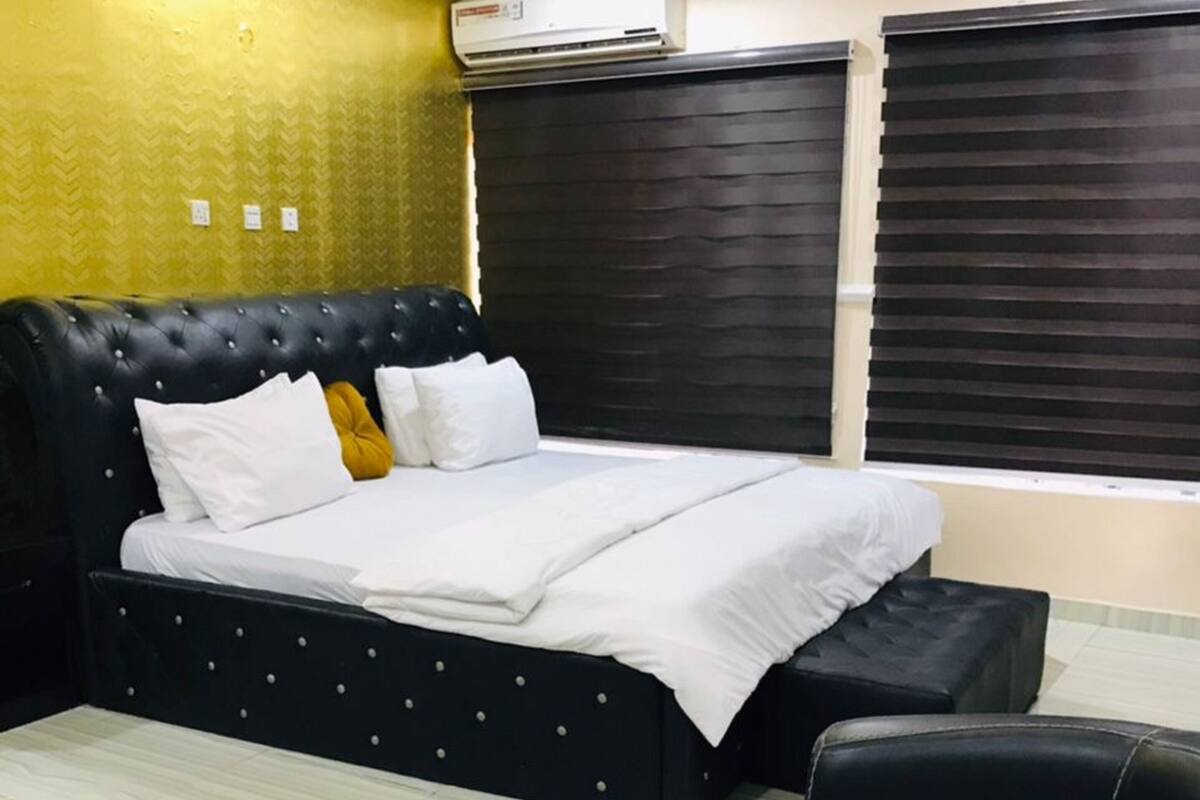 A bedroom with a black tufted headboard bed, white bedding, a black coffee table, and a black leather chair.