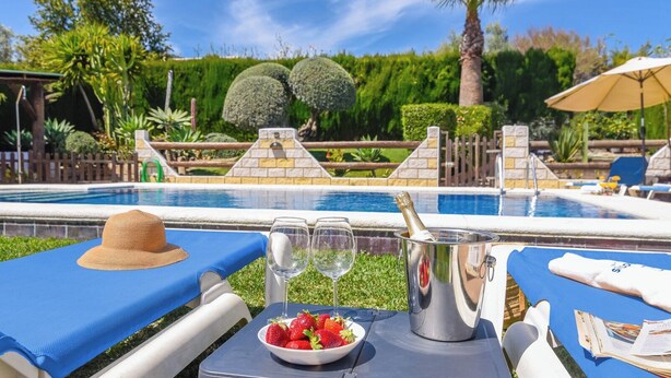 Un cadre agréable au bord de la piscine, avec une table dressée pour deux personnes, comprenant une bouteille de champagne, deux verres à vin, un saladier de fraises et un chapeau de paille.