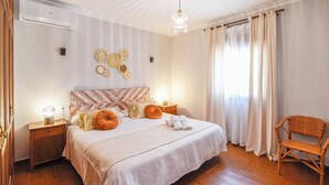 Une chambre à coucher bien rangée, avec un lit, des tables de chevet, une chaise et un climatiseur fixé au mur.