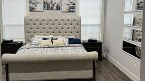 Een slaapkamer met een gestoffeerd hoofdeinde, een groot bed, een plafondventilator en kunst aan de muren.