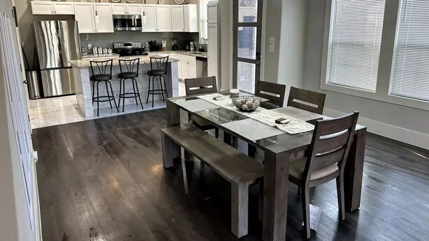 Een moderne keuken met witte kastjes, roestvrijstalen apparatuur en een eethoek met een houten tafel en stoelen.