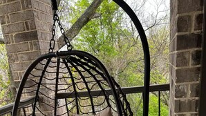 Een hangstoel met kussen in een kamer met bakstenen muren en een balkon.