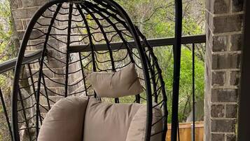 A hanging chair with a cushion in a room with brick walls and a balcony.